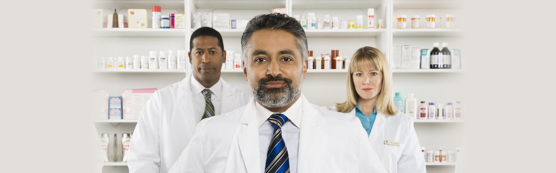 Portrait of a confident male pharmacist standing with two colleagues at pharmacy