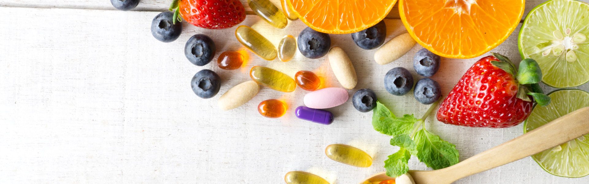 Multivitamins and supplements with fresh and healthy fruits on white wooden background